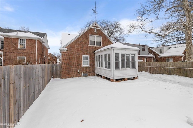 snow covered house with a sunroom, a fenced backyard, and brick siding