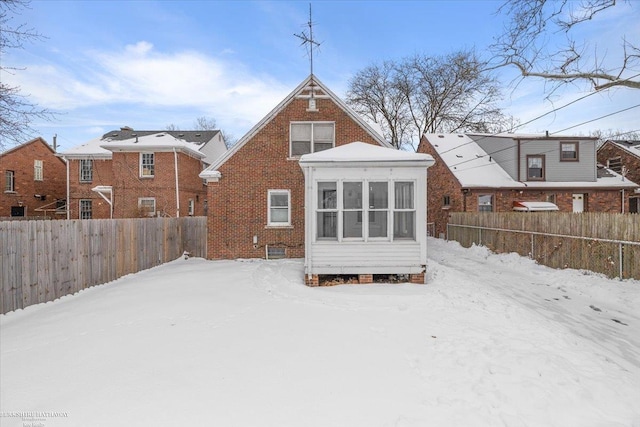 snow covered rear of property featuring brick siding and fence private yard