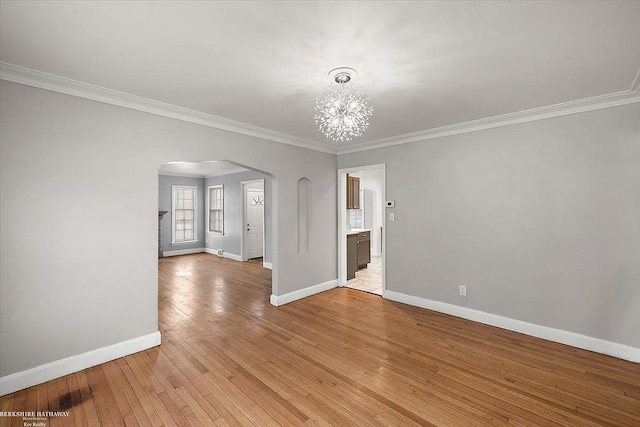 unfurnished room featuring arched walkways, light wood finished floors, ornamental molding, and baseboards