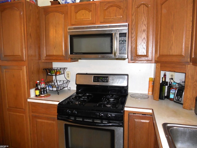 kitchen featuring a sink, stainless steel appliances, brown cabinetry, and light countertops