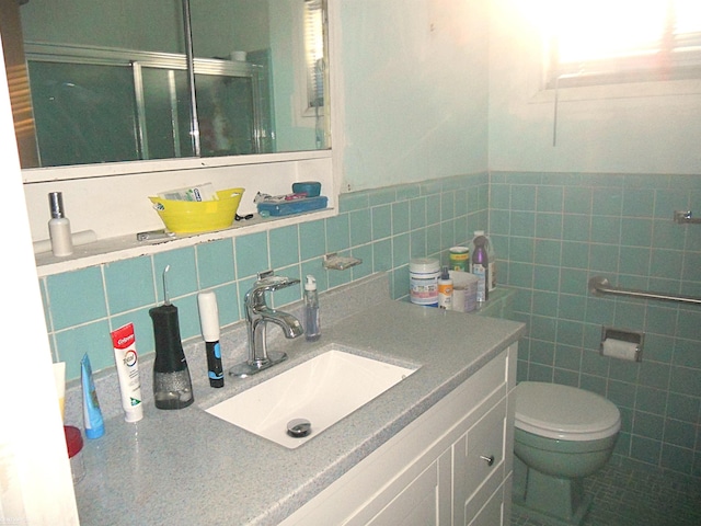 bathroom with tile walls, toilet, a shower stall, and vanity