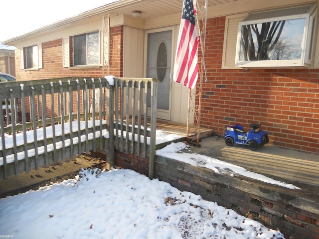 snow covered property entrance featuring brick siding