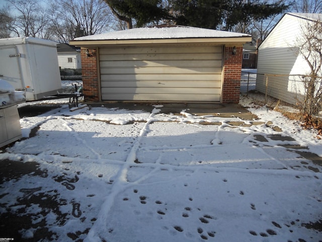 snow covered garage featuring a garage and fence