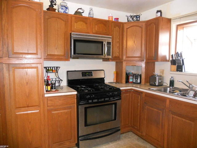 kitchen featuring a sink, brown cabinetry, stainless steel appliances, and light countertops