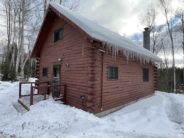 view of snow covered exterior featuring log exterior and a chimney