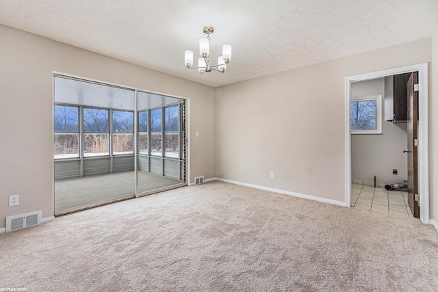 spare room featuring visible vents, a notable chandelier, light carpet, and a textured ceiling