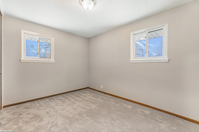 spare room featuring light carpet, a wealth of natural light, and baseboards