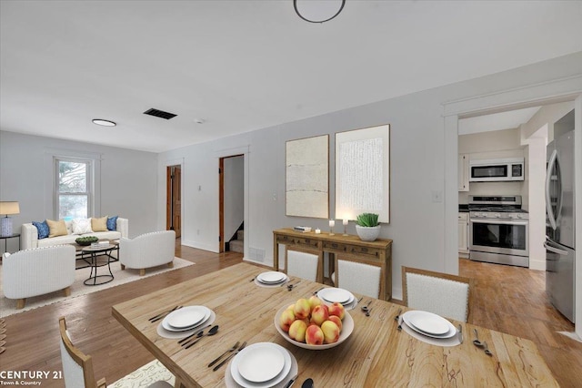 dining room with light wood finished floors, visible vents, stairway, and baseboards