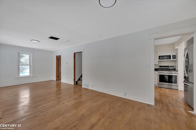 unfurnished room with baseboards, visible vents, stairway, and light wood finished floors