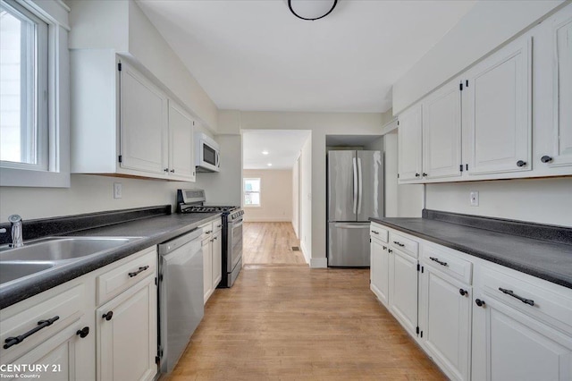 kitchen with dark countertops, light wood-style flooring, appliances with stainless steel finishes, white cabinetry, and a sink