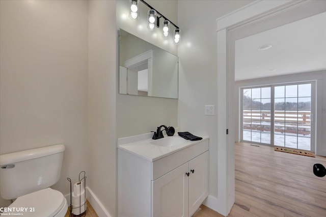 half bathroom featuring baseboards, vanity, toilet, and wood finished floors