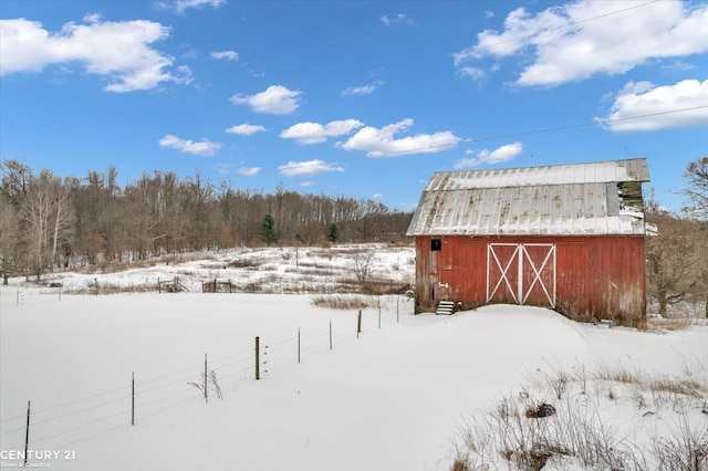 snowy yard with a garage, an outdoor structure, and a barn