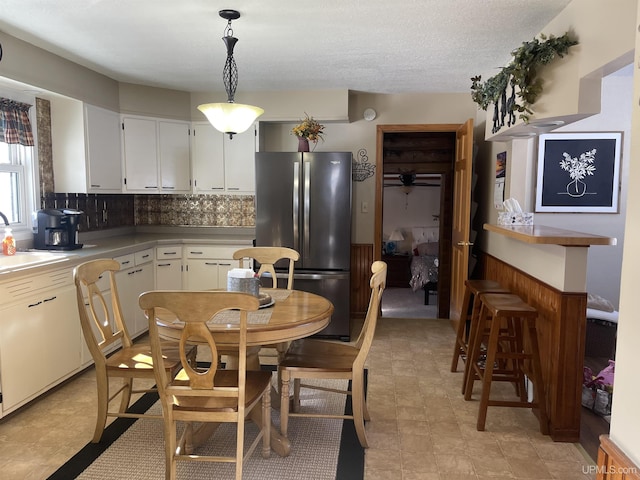 kitchen featuring white cabinets, freestanding refrigerator, hanging light fixtures, light countertops, and a sink