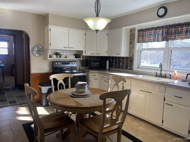 kitchen with arched walkways, light countertops, white cabinetry, pendant lighting, and a sink