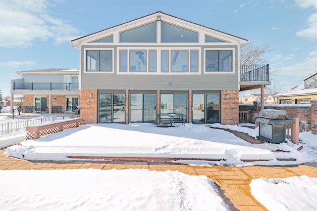 snow covered back of property featuring a balcony and brick siding