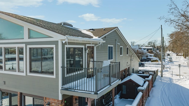 view of snow covered exterior with roof with shingles, brick siding, and a balcony