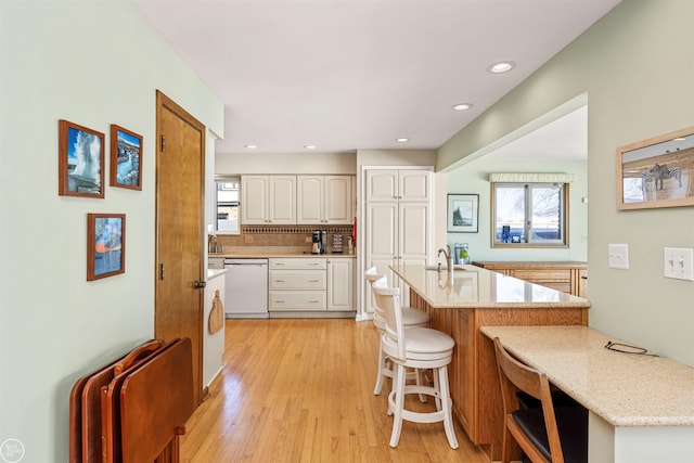 kitchen featuring a breakfast bar, a sink, white cabinetry, light stone countertops, and dishwasher