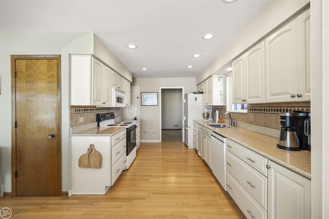 kitchen featuring white appliances, white cabinets, light stone countertops, light wood-style floors, and a sink