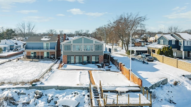 snow covered rear of property with a residential view and fence