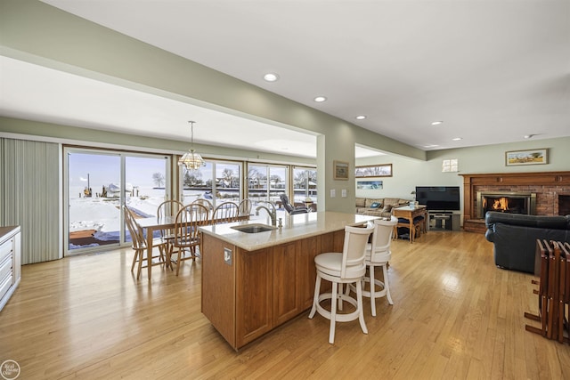 kitchen with a center island with sink, hanging light fixtures, light stone countertops, light wood-type flooring, and a sink