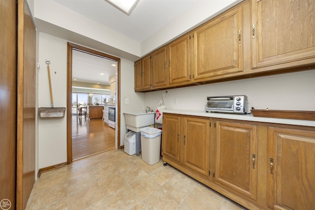 kitchen featuring baseboards, light countertops, brown cabinetry, and a toaster