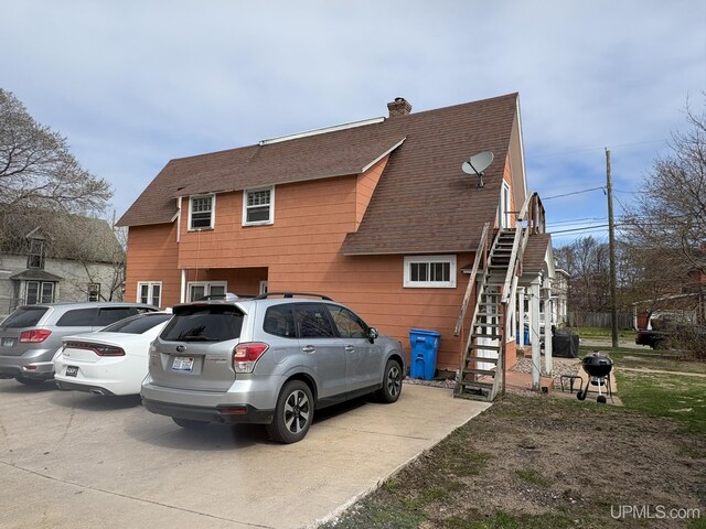 view of home's exterior featuring stairway, a shingled roof, and a chimney
