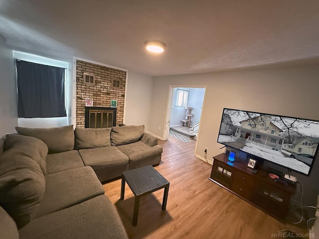 living area featuring baseboards, light wood-type flooring, and a brick fireplace