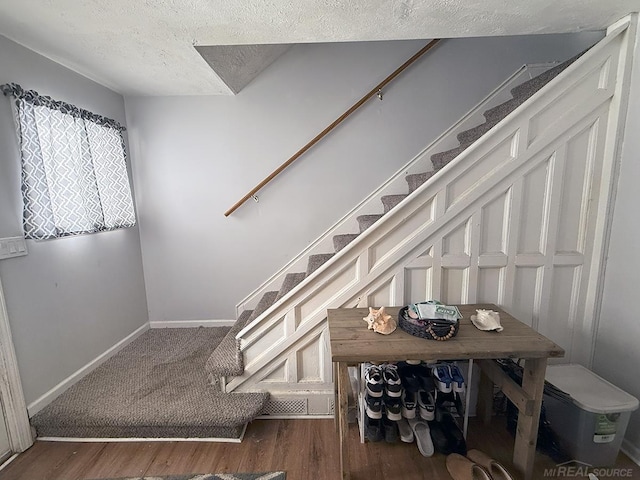 staircase featuring a textured ceiling, wood finished floors, and baseboards