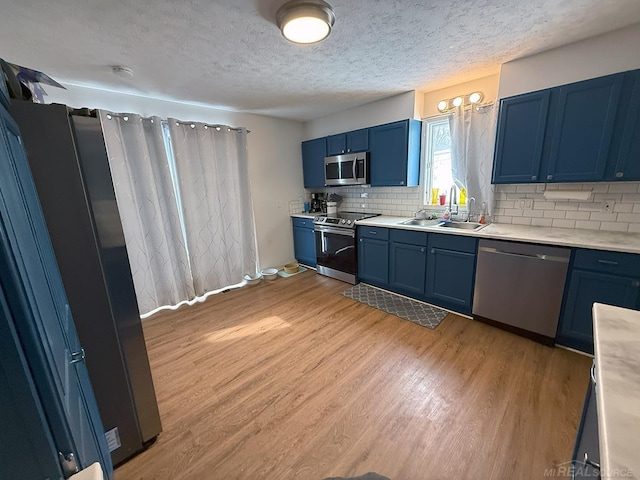 kitchen featuring light wood finished floors, blue cabinets, stainless steel appliances, light countertops, and a sink