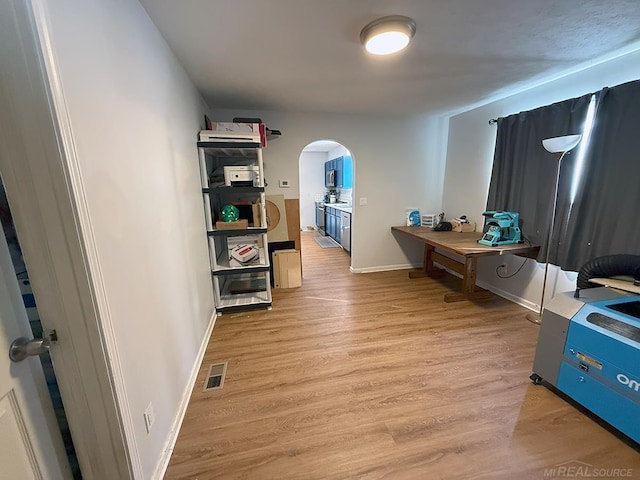 hallway featuring arched walkways, baseboards, visible vents, and light wood-style floors