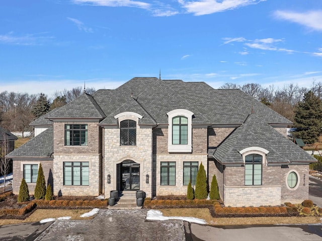 french country style house with a shingled roof and brick siding