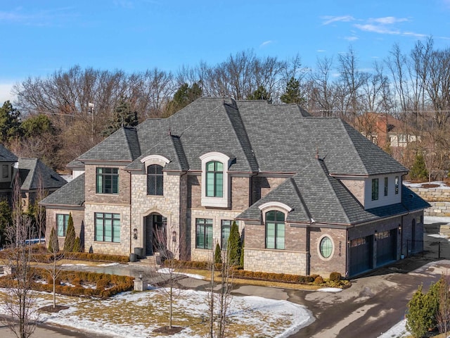 french country inspired facade featuring aphalt driveway, roof with shingles, brick siding, and a garage