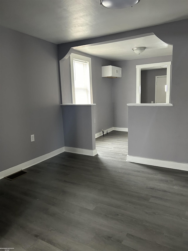 unfurnished room with dark wood finished floors, visible vents, and baseboards