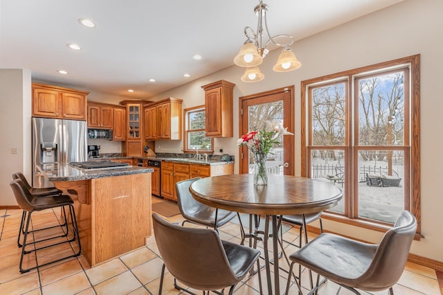 kitchen with a center island, hanging light fixtures, glass insert cabinets, appliances with stainless steel finishes, and dark stone counters