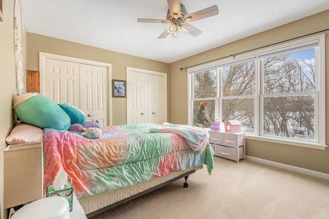 carpeted bedroom featuring ceiling fan, two closets, and baseboards