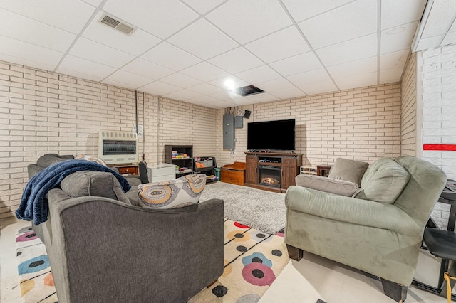 living area featuring a warm lit fireplace, visible vents, brick wall, heating unit, and a paneled ceiling