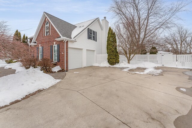 view of side of property featuring driveway, a chimney, an attached garage, fence, and brick siding