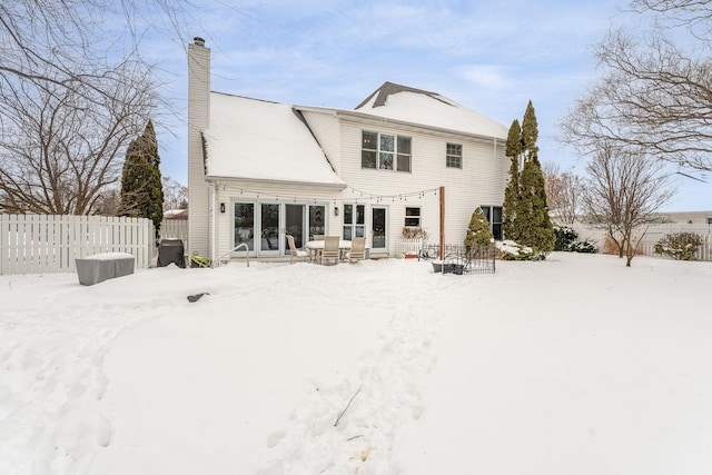 snow covered rear of property featuring fence and a chimney