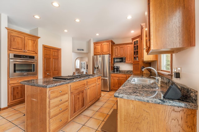 kitchen featuring brown cabinetry, glass insert cabinets, appliances with stainless steel finishes, a center island, and a sink