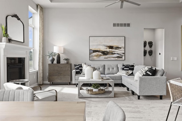 living room with light colored carpet, a glass covered fireplace, visible vents, and a ceiling fan