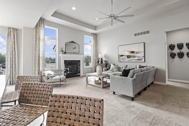 carpeted living area with baseboards, visible vents, a raised ceiling, a glass covered fireplace, and recessed lighting