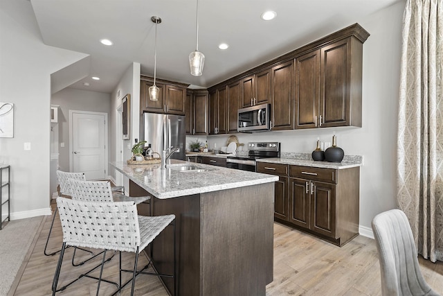 kitchen with stainless steel appliances, a sink, hanging light fixtures, dark brown cabinets, and light stone countertops