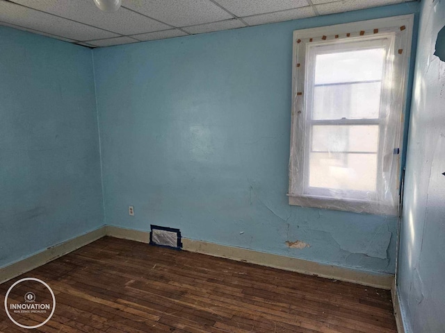 empty room featuring dark wood-style floors, a paneled ceiling, and baseboards