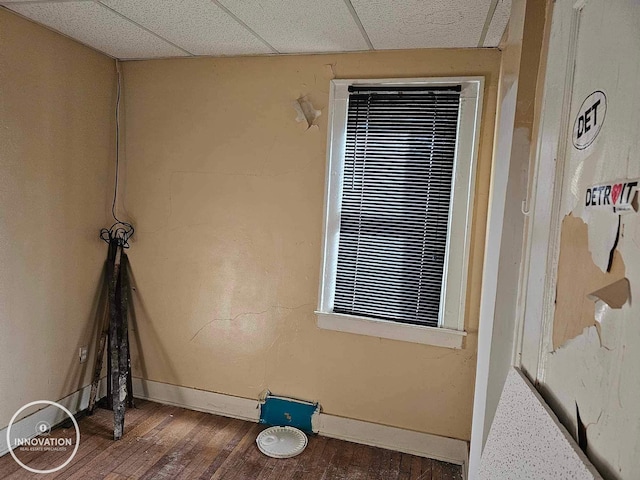 empty room featuring a paneled ceiling, dark wood-style flooring, and baseboards