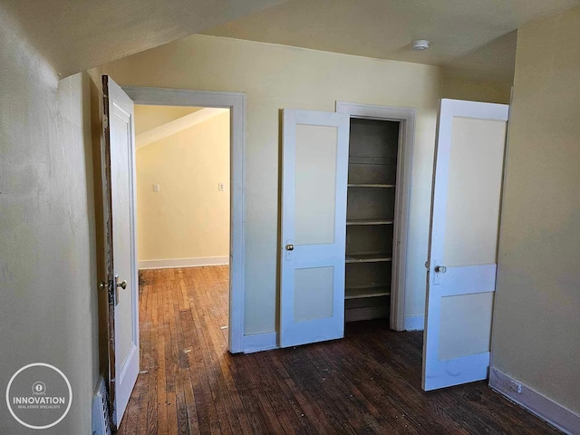 unfurnished bedroom with baseboards and dark wood-type flooring