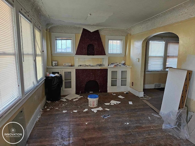 unfurnished living room featuring dark wood-style floors, arched walkways, and visible vents