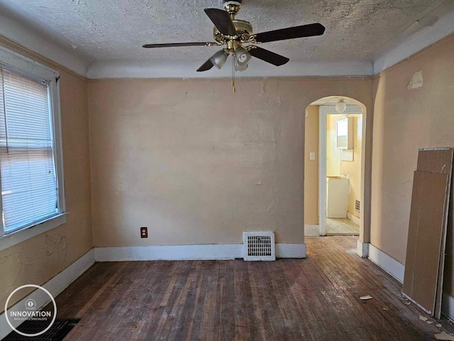 unfurnished room with arched walkways, a textured ceiling, visible vents, baseboards, and dark wood finished floors