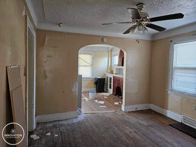 unfurnished room with a textured ceiling, baseboards, arched walkways, and wood finished floors