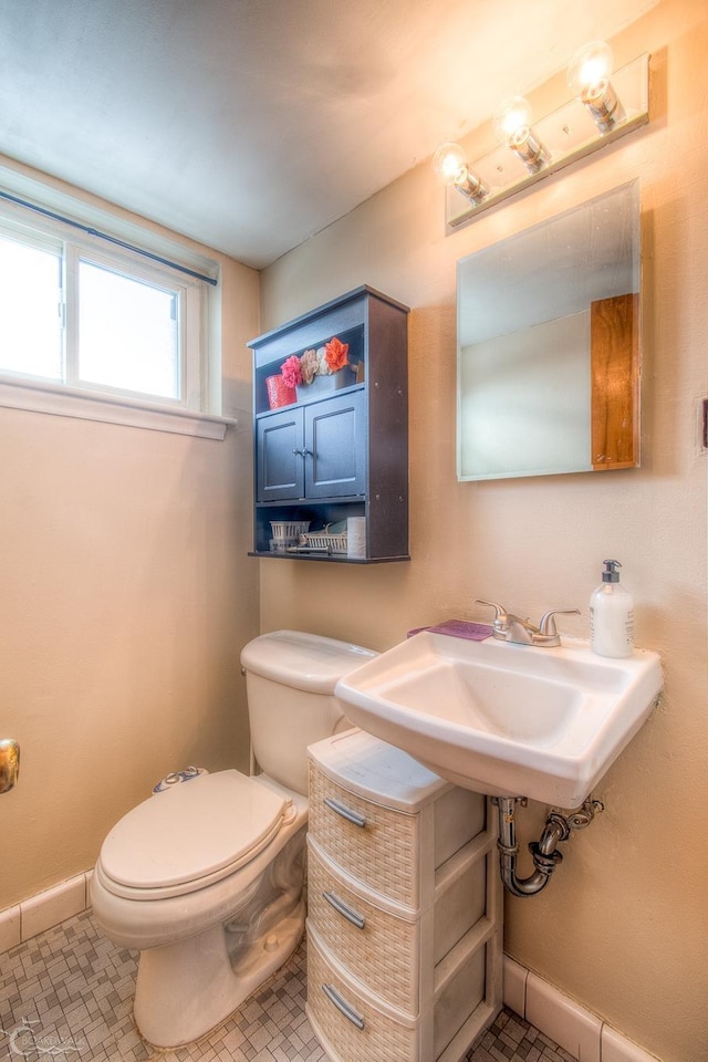 half bathroom featuring tile patterned floors, a sink, toilet, and baseboards