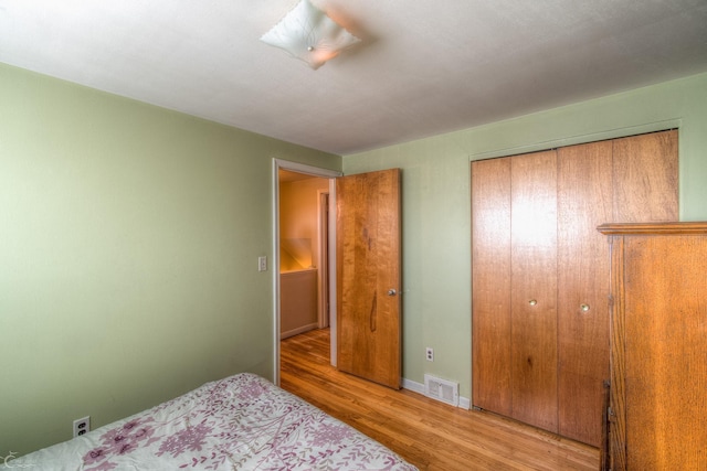 bedroom with light wood-type flooring, a closet, visible vents, and baseboards